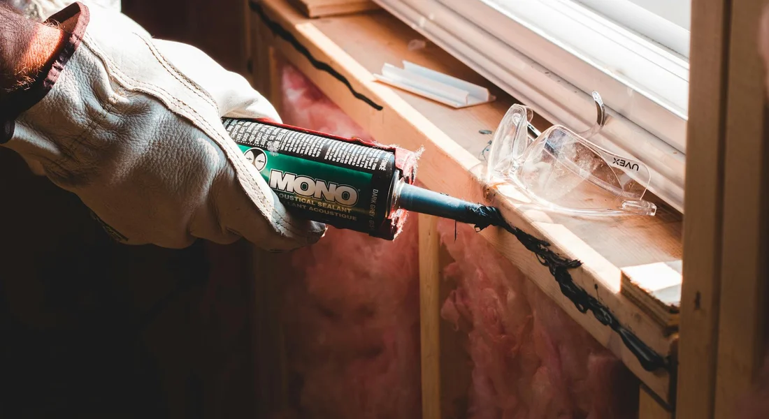 Gloved hand using a caulking gun to apply sealant along a car window frame