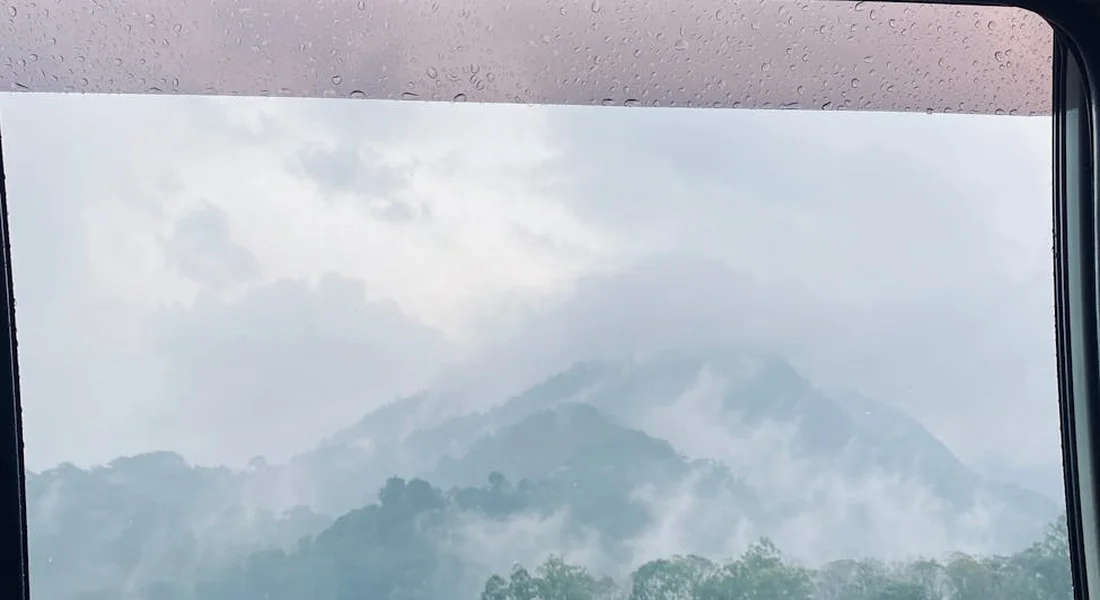 Foggy car windshield with condensation, offering a view of misty mountains outside.