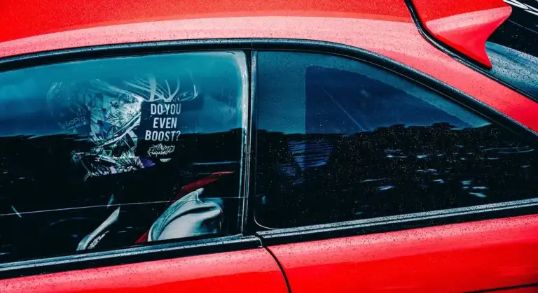 Close-up of a red car window with a decal that reads 'DO YOU EVEN BOOST?' on the glass.