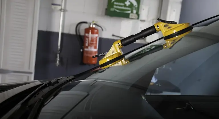 Windshield in a repair shop with a yellow repair tool attached to the glass.