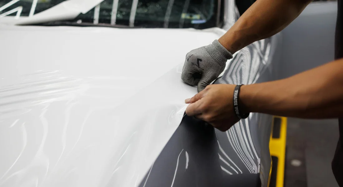 Close-up of hands wearing gloves applying car wrap vinyl to a vehicle panel