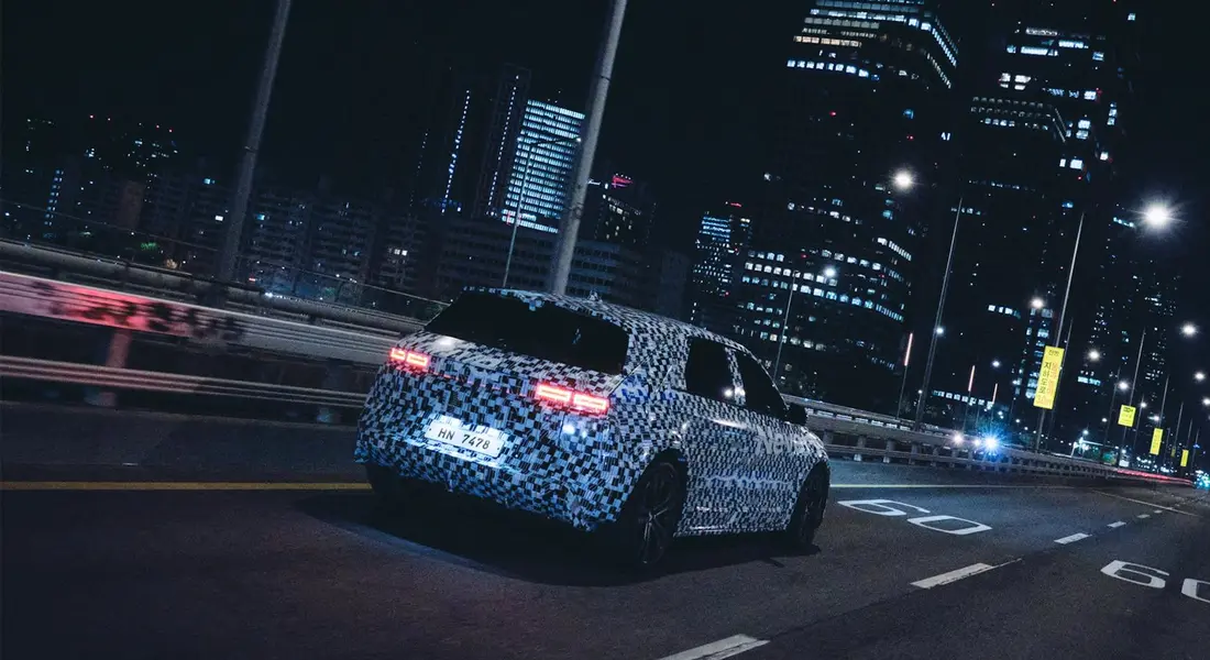 A car wrapped in a blue camouflage pattern driving on a city highway at night, illuminated by streetlights and tall buildings.