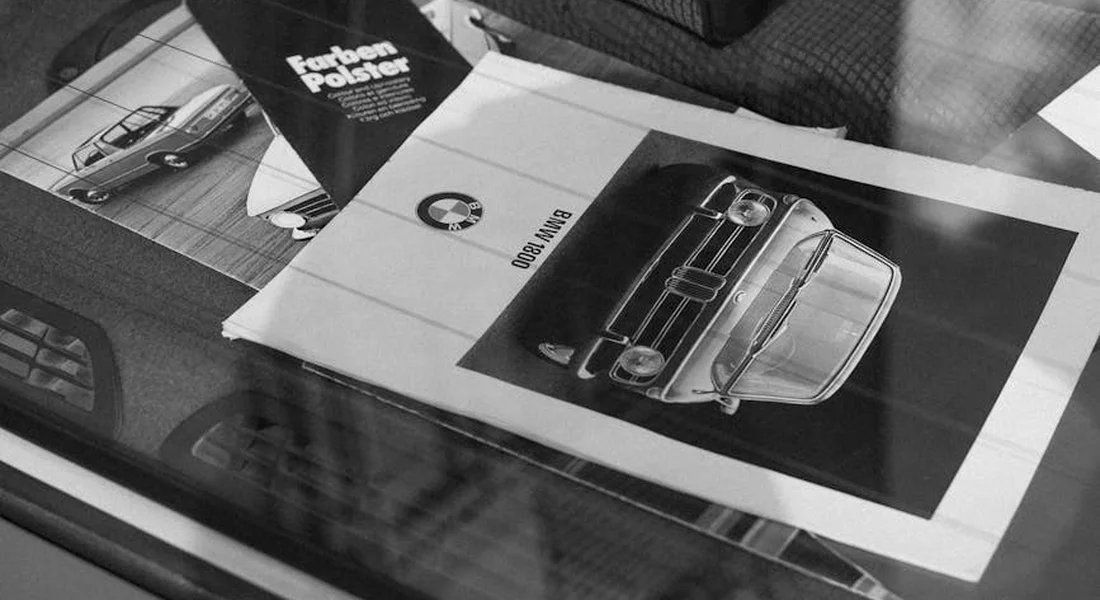 Black-and-white photograph of car brochures spread on a car seat inside a vehicle.