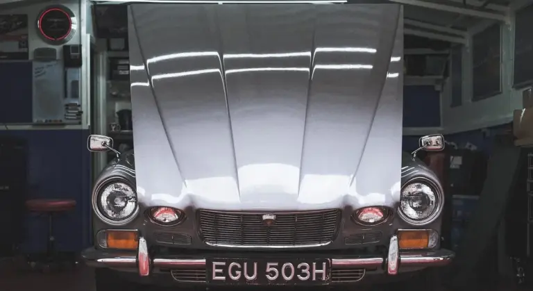 Front view of a vintage car in a workshop, showing the chrome bumper and headlights.