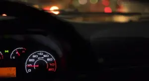 Close-up of a car dashboard with illuminated gauges at night.