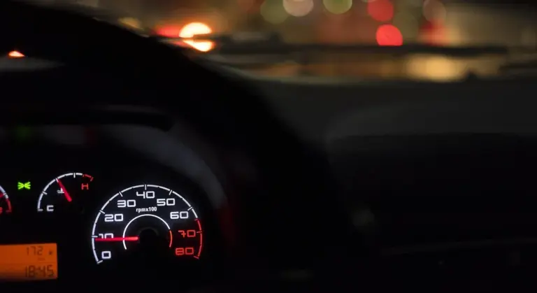 Close-up of a car dashboard with illuminated gauges at night.