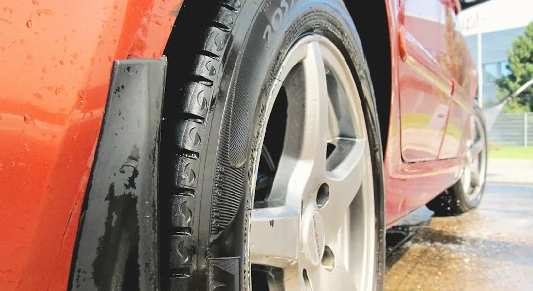 Close-up of an orange car wheel and tire with water droplets, highlighting the car detailing context