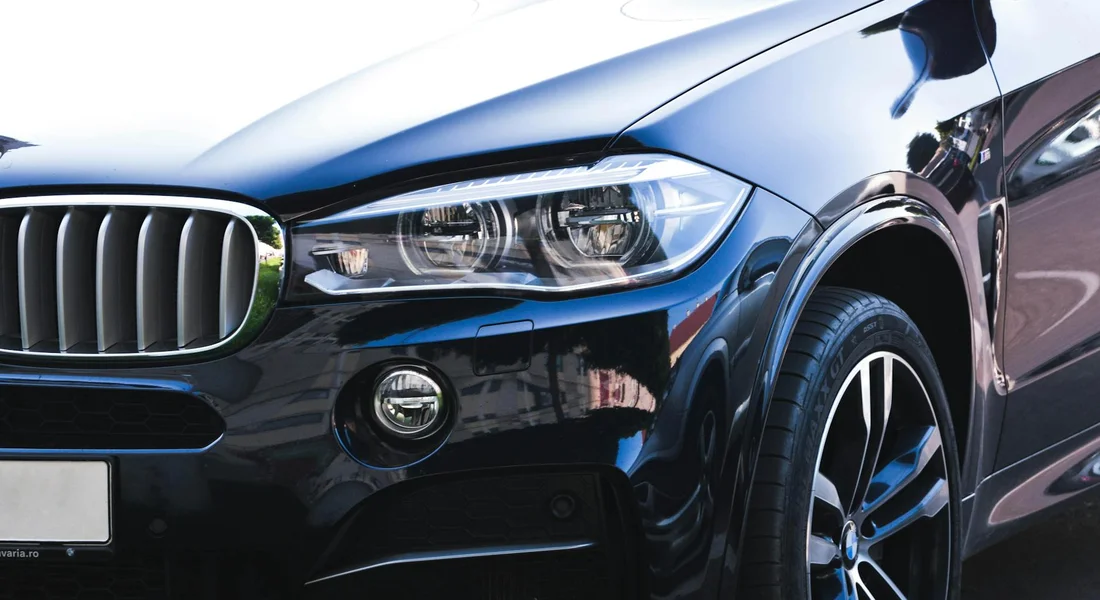 Close-up of a sleek dark blue car front end with a prominent headlight, grille, and wheel.