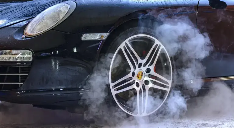 Close-up of a black Porsche wheel with smoke around the tire.