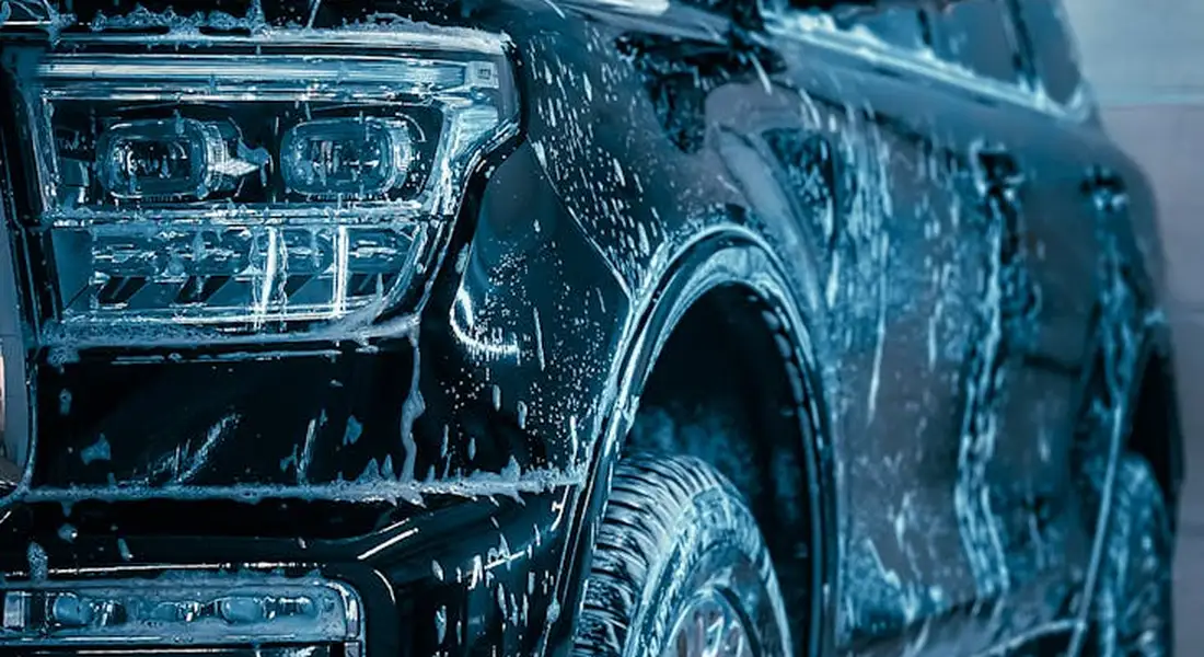 Dark blue SUV with soap suds covering its surface, front-left wheel visible.
