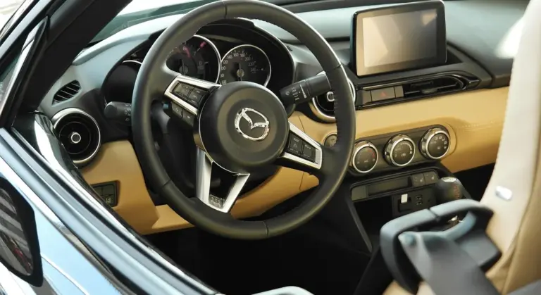 Interior of a car with a steering wheel, instrument cluster, and center console, featuring beige and black accents.