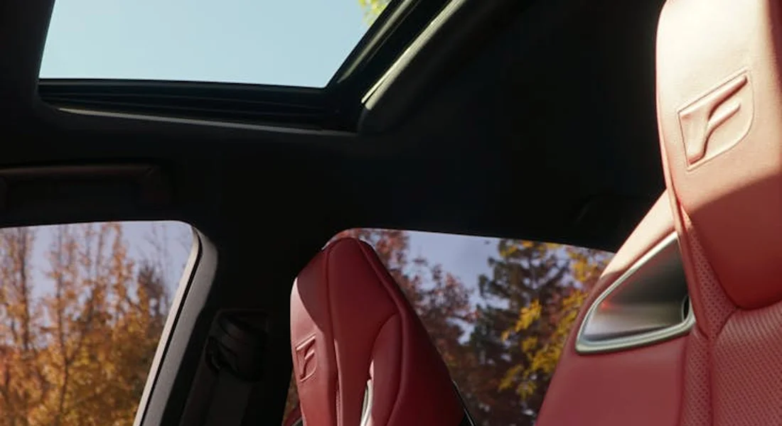 Red leather car seats with an open sunroof and autumn trees visible through the windows.