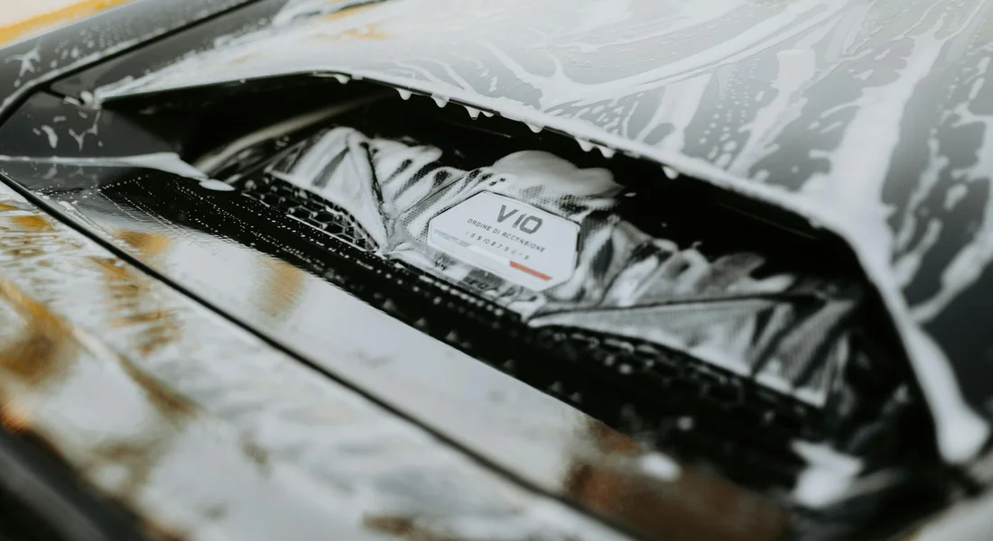 Close-up of a car's black paint surface with water spots and soap streaks on the hood.
