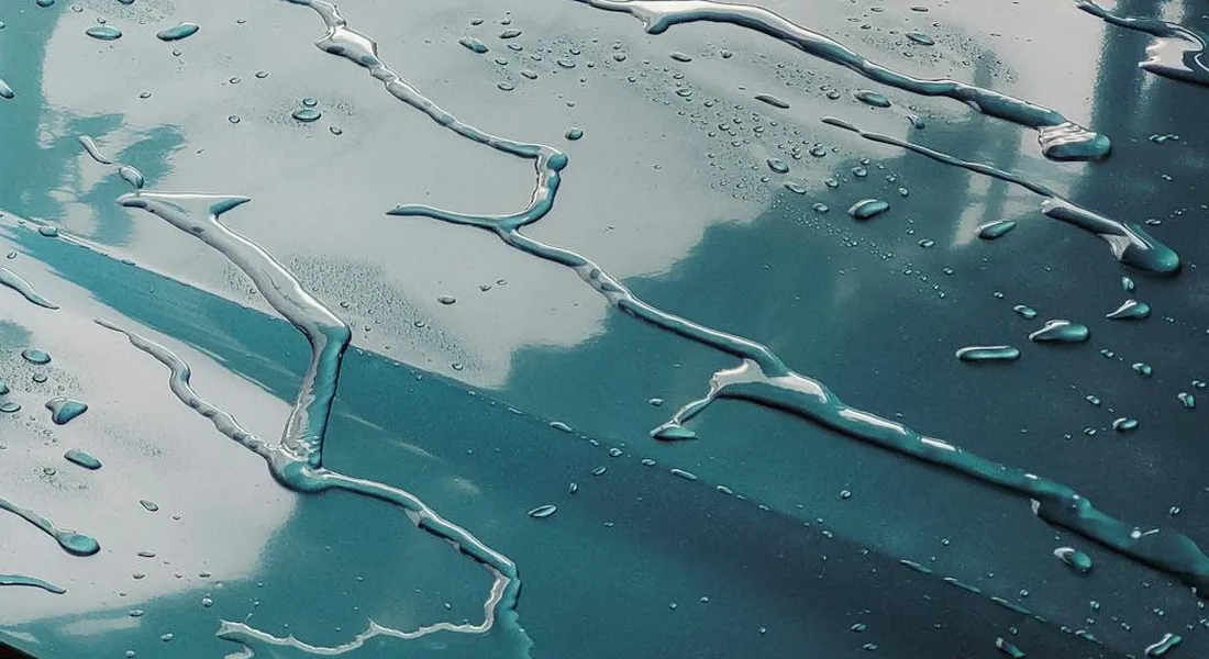 Close-up of a car's glossy teal paint with water droplets and streaks