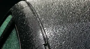 Close-up of a glossy black car panel with numerous water droplets on the surface.