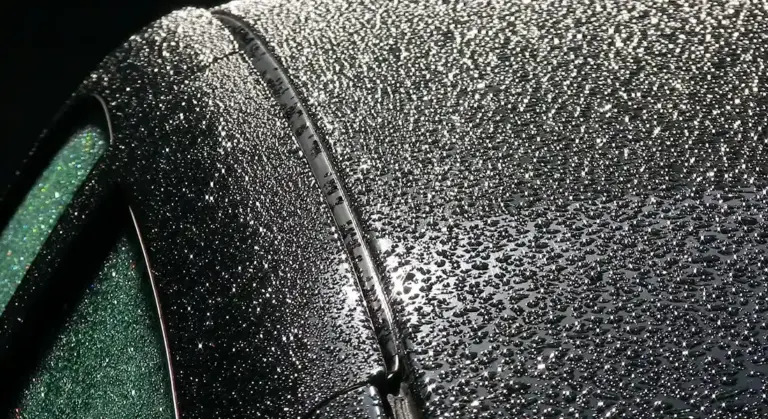 Close-up of a glossy black car panel with numerous water droplets on the surface.