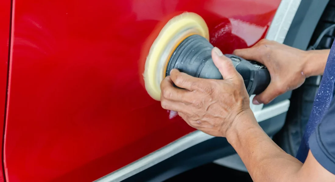 Person holding a polishing buffer and buffing a red car door to protect the paint