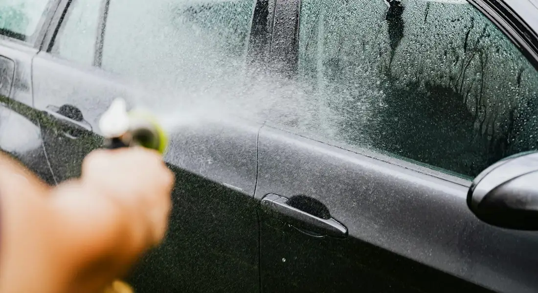 A person using a spray bottle on the side of a dark car, illustrating the point where DIY paint spot removal might fail and professional help may be needed.