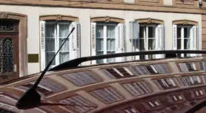 Close-up of a glossy car hood with a windshield wiper, reflecting the facade of a row of windows and buildings.