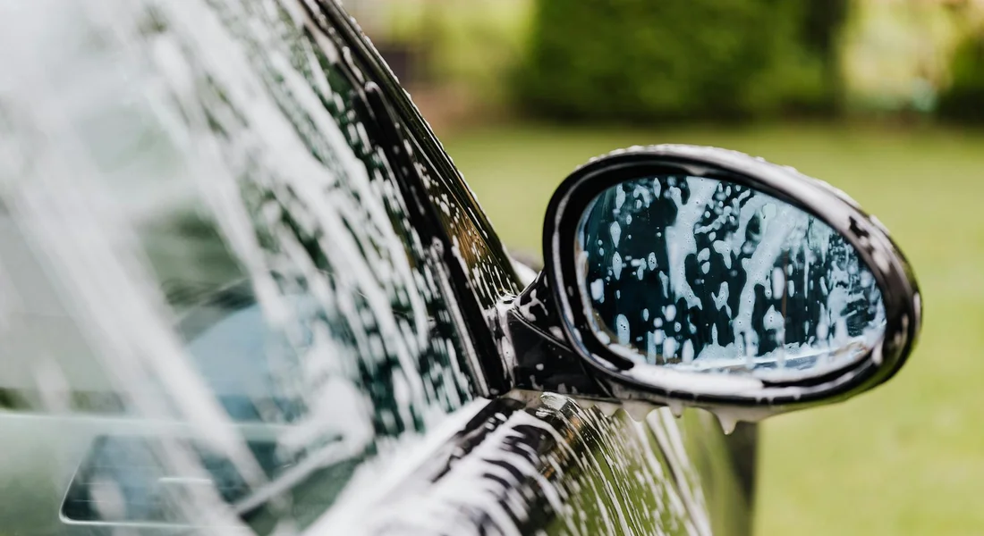 Close-up of a car's side mirror and door with white spray paint splatters, illustrating the challenge of removing graffiti without harming the finish.