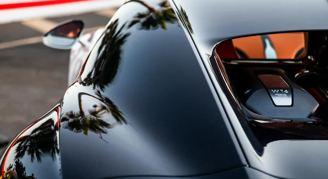 Close-up of a glossy black car panel reflecting palm trees, illustrating a clean, well-prepared surface ready for paint blending.