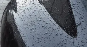 Close-up of a car's glossy black paint with numerous water droplets