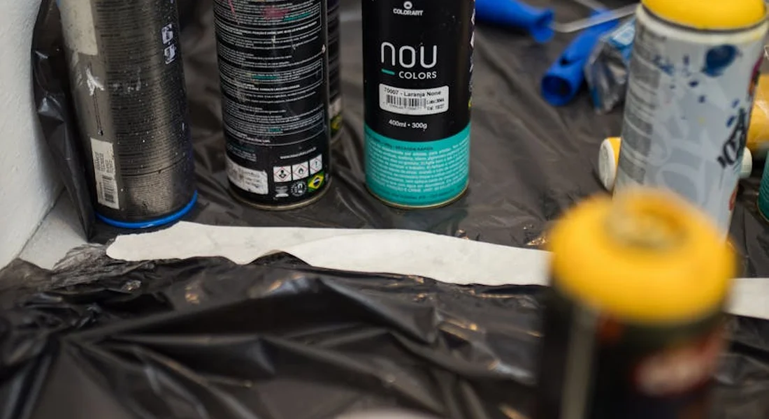 Workshop scene with spray paint cans, a protected work surface, and masking materials set up for automotive finishing, illustrating the cutting and polishing stage after curing.