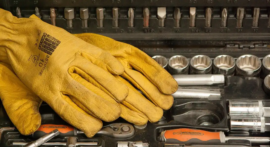 Yellow work glove resting on a toolbox filled with sockets, wrenches, and screwdrivers—ready for automotive sanding prep.