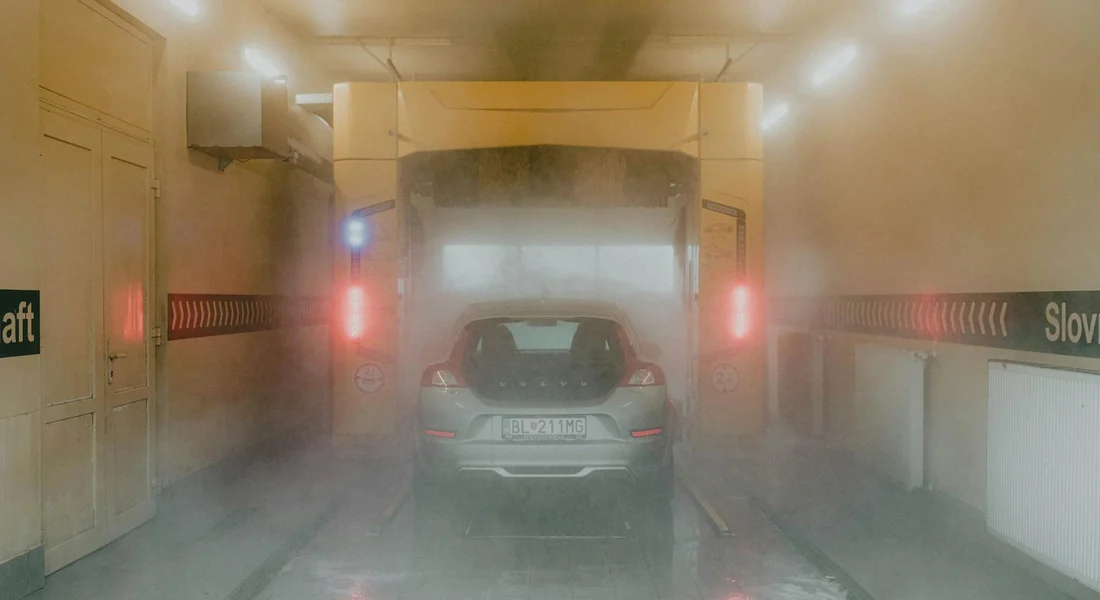 A car inside a paint spray booth with spray mist filling the air, focusing on exterior surfaces