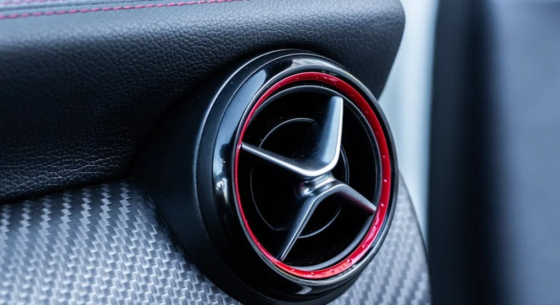 Close-up of a circular car air vent with black interior and red trim, set in a textured dashboard.