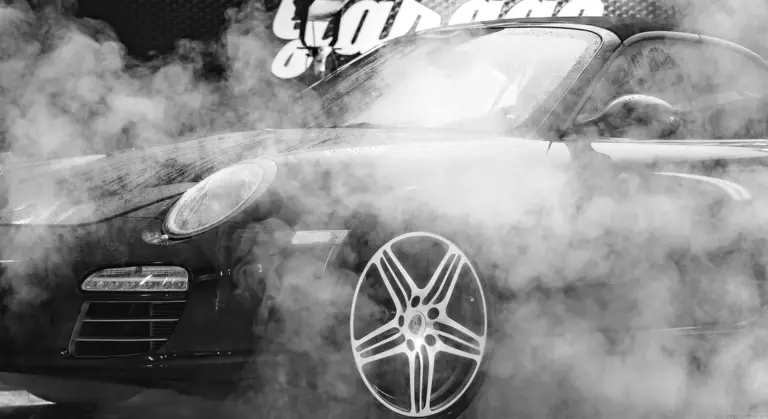 Black and white photo of a sleek sports car surrounded by steam during a car wash.