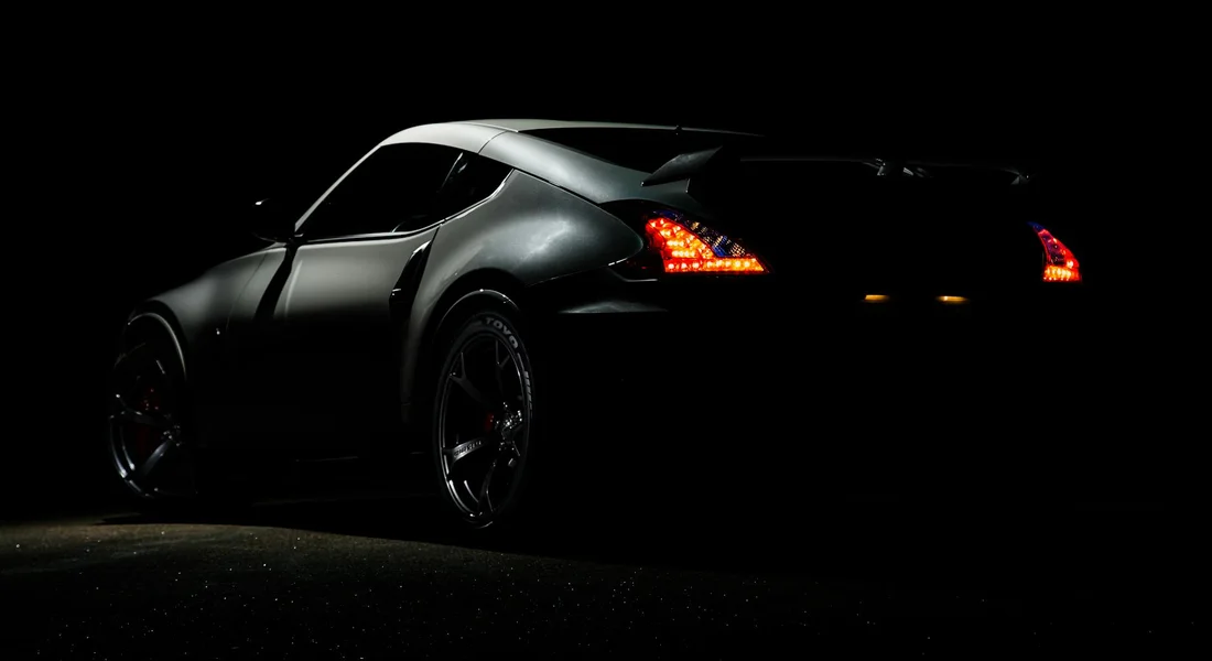 Rear three-quarter view of a dark sports car at night with illuminated taillights