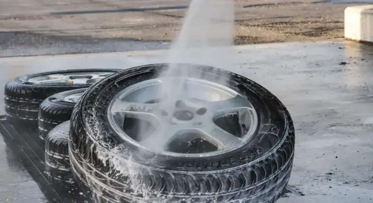 A car wheel being rinsed with water spray and soap suds around the tire at a car wash.