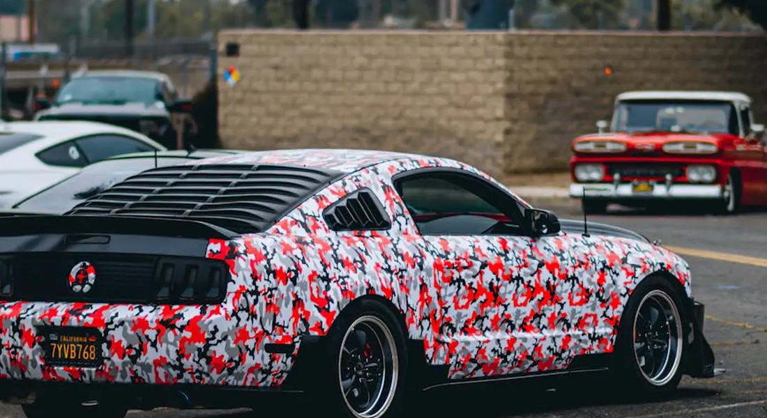 A sports car covered in a bold camouflage wrap parked in a lot.
