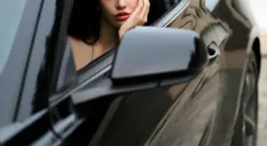 A close-up of a glossy black car door and side mirror with a woman looking out from the window.