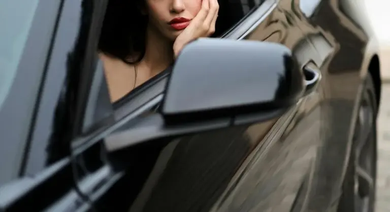 A close-up of a glossy black car door and side mirror with a woman looking out from the window.