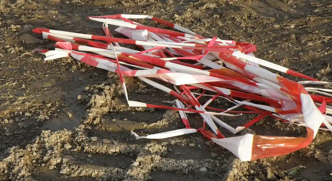 Red and white caution tape tangled on a muddy dirt surface