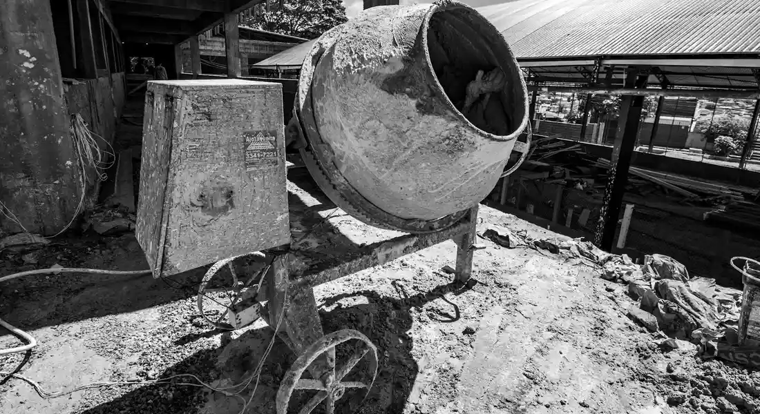 Black-and-white photo of a cement mixer on a construction site with a pile of cement and debris on the ground