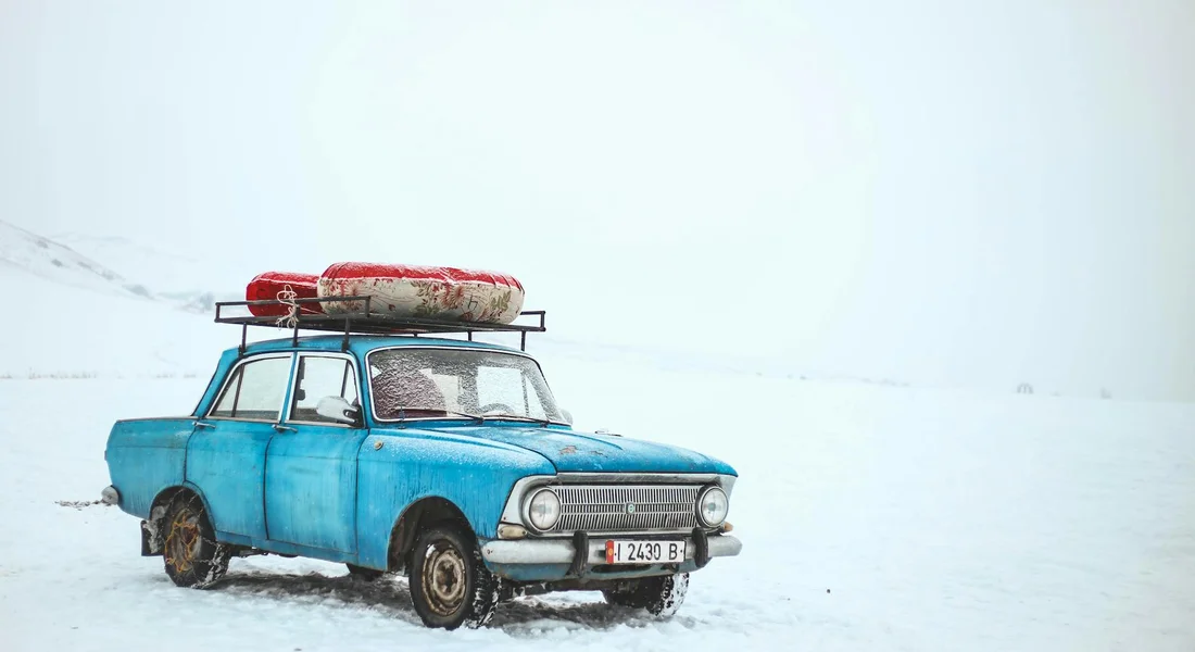 Retro blue car with surfboards on the roof parked in a snowy landscape
