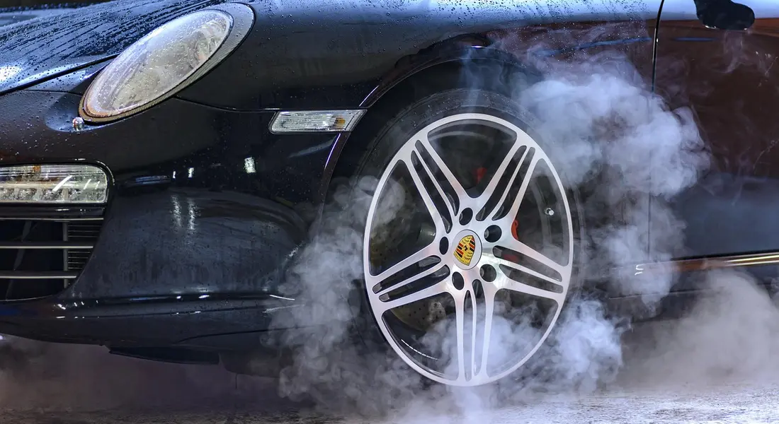 Black sports car front wheel with a Porsche emblem, smoke rising around the tire