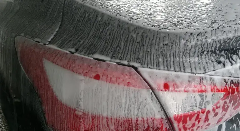 Rear end of a red car covered in soap suds during a wash