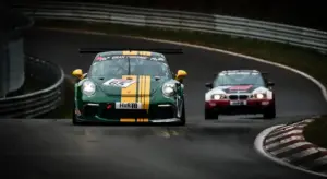 Green vintage race car with a yellow racing stripe on a winding race track, with a red car behind.