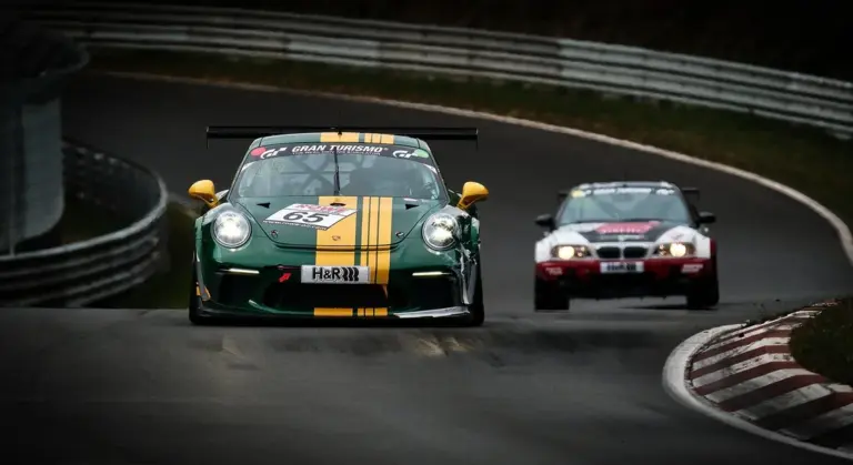 Green vintage race car with a yellow racing stripe on a winding race track, with a red car behind.