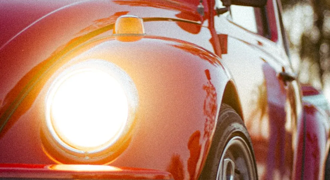 Close-up of a red vintage car's front fender and headlight with sunlight reflecting off the glossy paint.