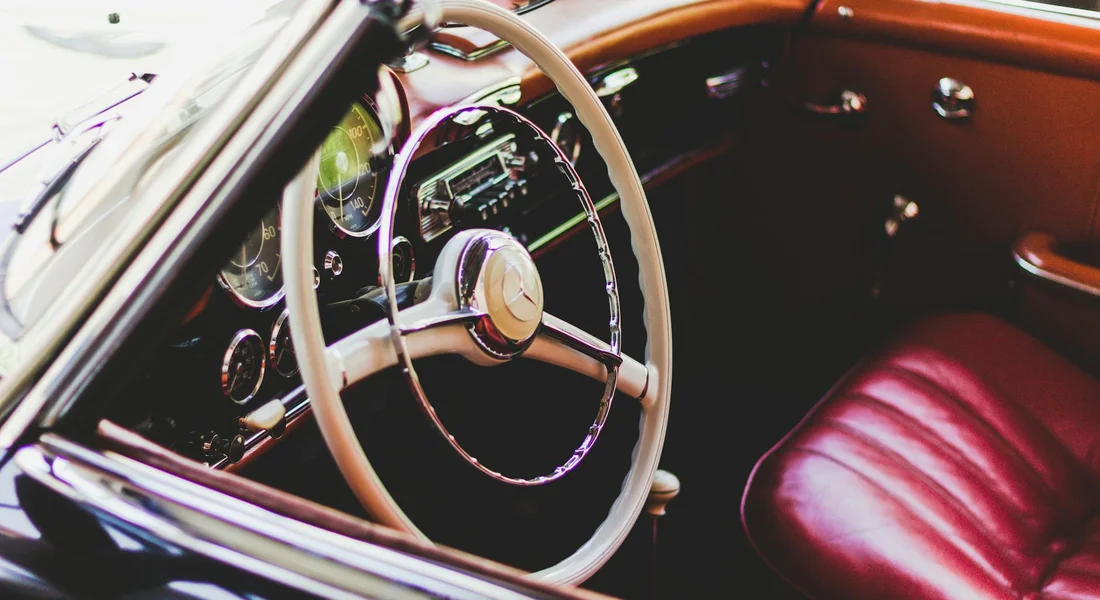 Close-up of a vintage car interior with a cream steering wheel and red leather seats, illustrating leather conditioning and protection.