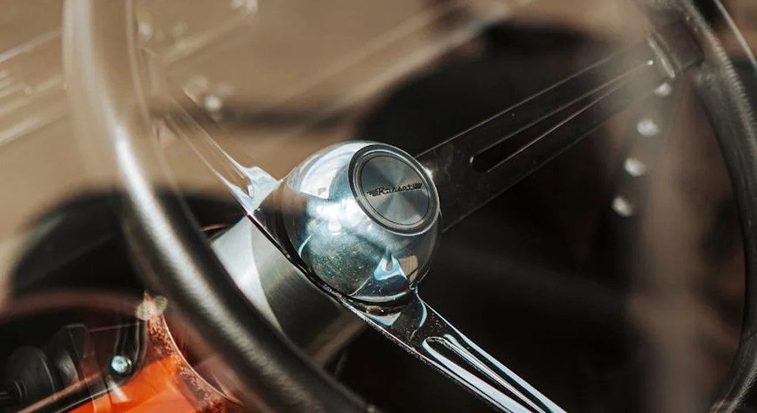 Close-up view of a classic car steering wheel and interior seen through glass, highlighting glossy surfaces where wax can accumulate.