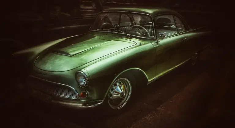 A vintage green car in a dimly lit setting, highlighting smooth paint and chrome details.