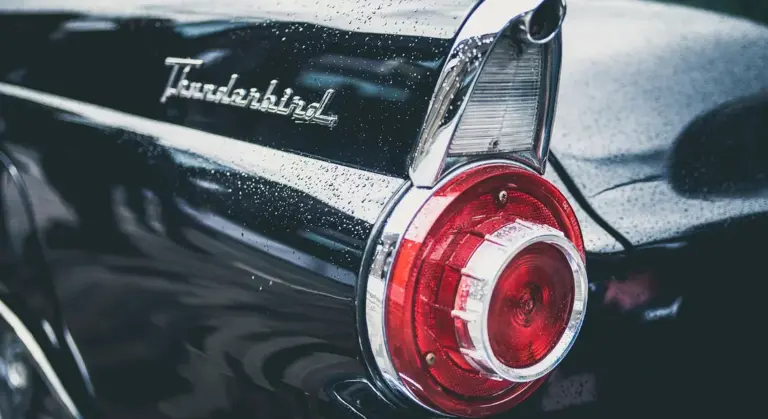 Rear end of a black vintage Ford Thunderbird with chrome trim and a round red taillight, showing surface scratches