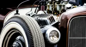 Close-up of a vintage car's front end featuring a wheel, headlight, and chrome grille.
