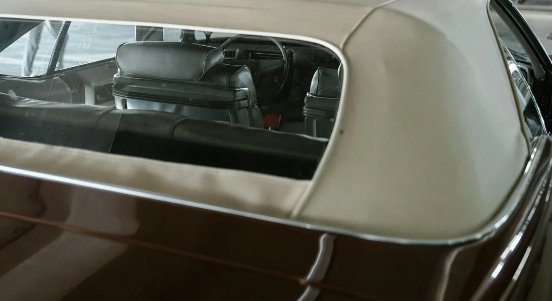 Rear interior of a vintage car featuring dark leather seats and a light tan headliner